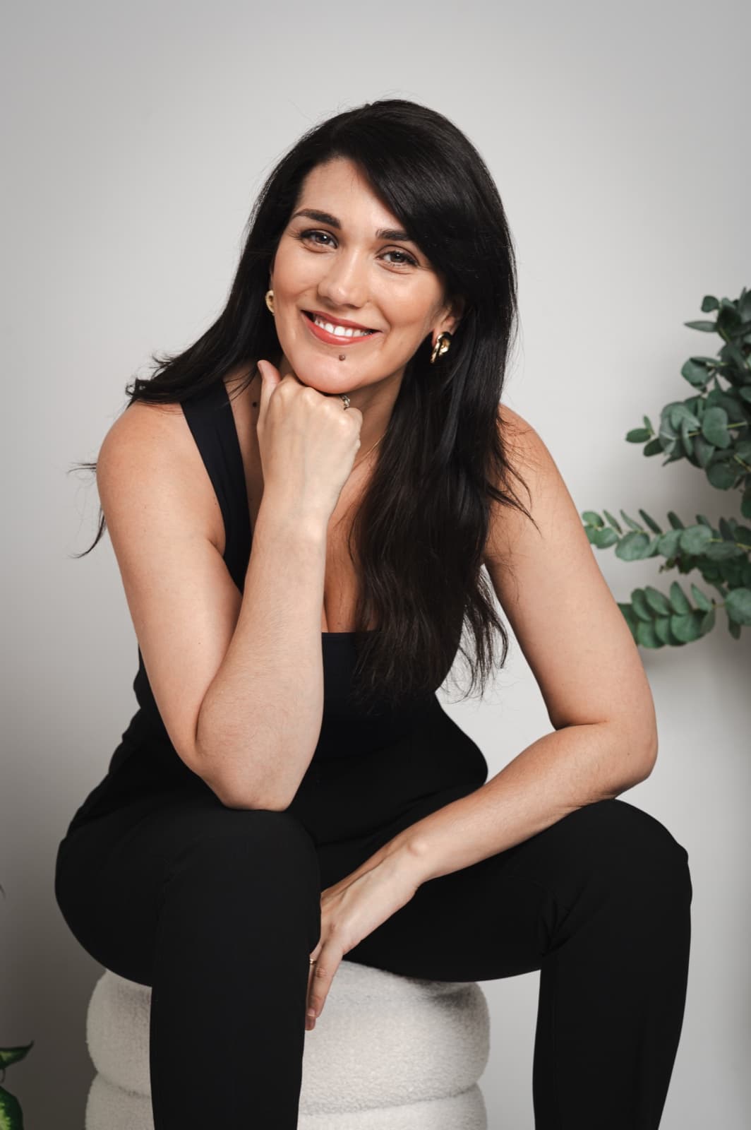 Isabel Fonseca seated on a white stool against a green foliage background